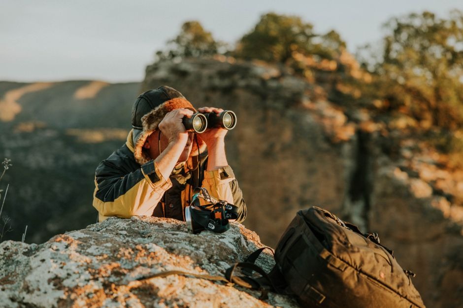 A photographer using a camera from a rocky overlook during warm evening light.