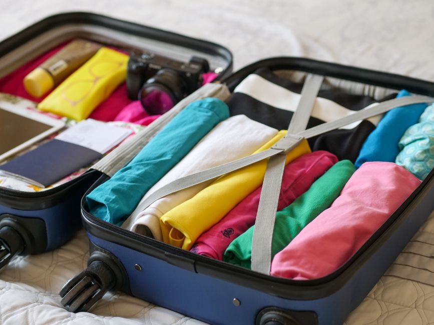 An open compact suitcase neatly packed with folded clothes and simple travel essentials.