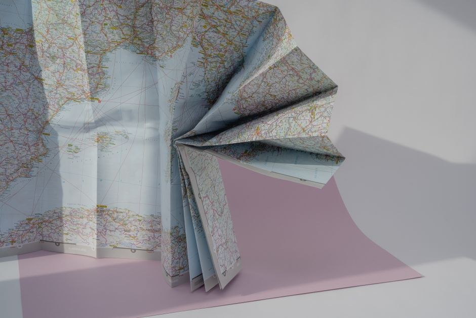 Folded paper maps arranged as a tactile still life, representing curiosity and careful exploration.